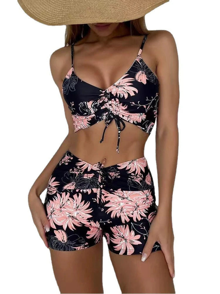 Vrouw in zomerse tweedelige set met roze bloemenprint en zwarte achtergrond, draagt een grote strohoed. Perfect voor strandmode en zomerse stijl.