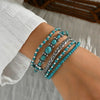 Set van 5 armbanden met turquoise kralen en zilverkleurige details.